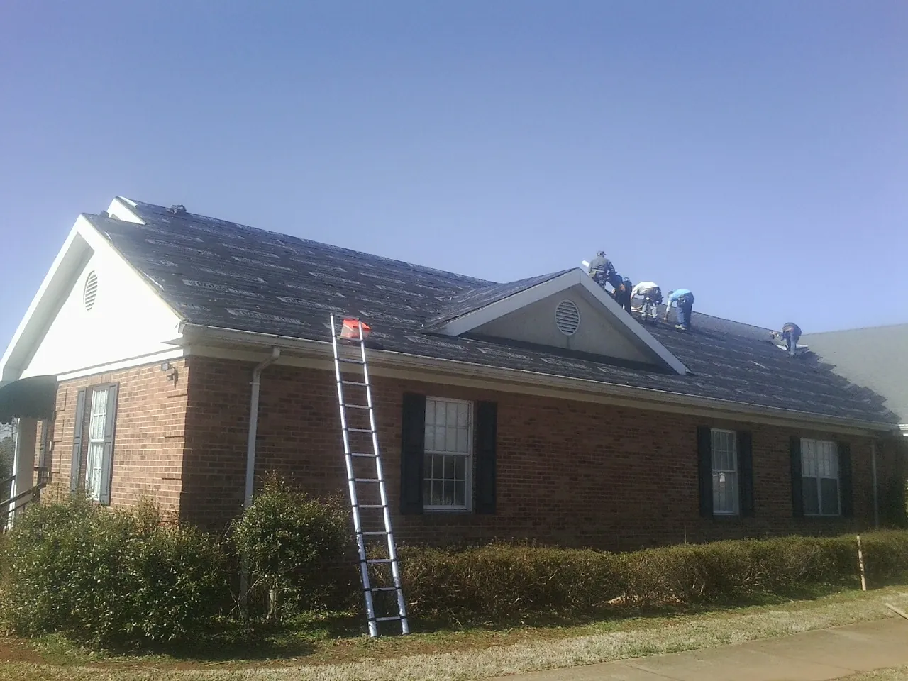 Crew tearing shingles off a brick ranch roof with a ladder set — Emergency Roof Repair work by our crew in Eastanollee
