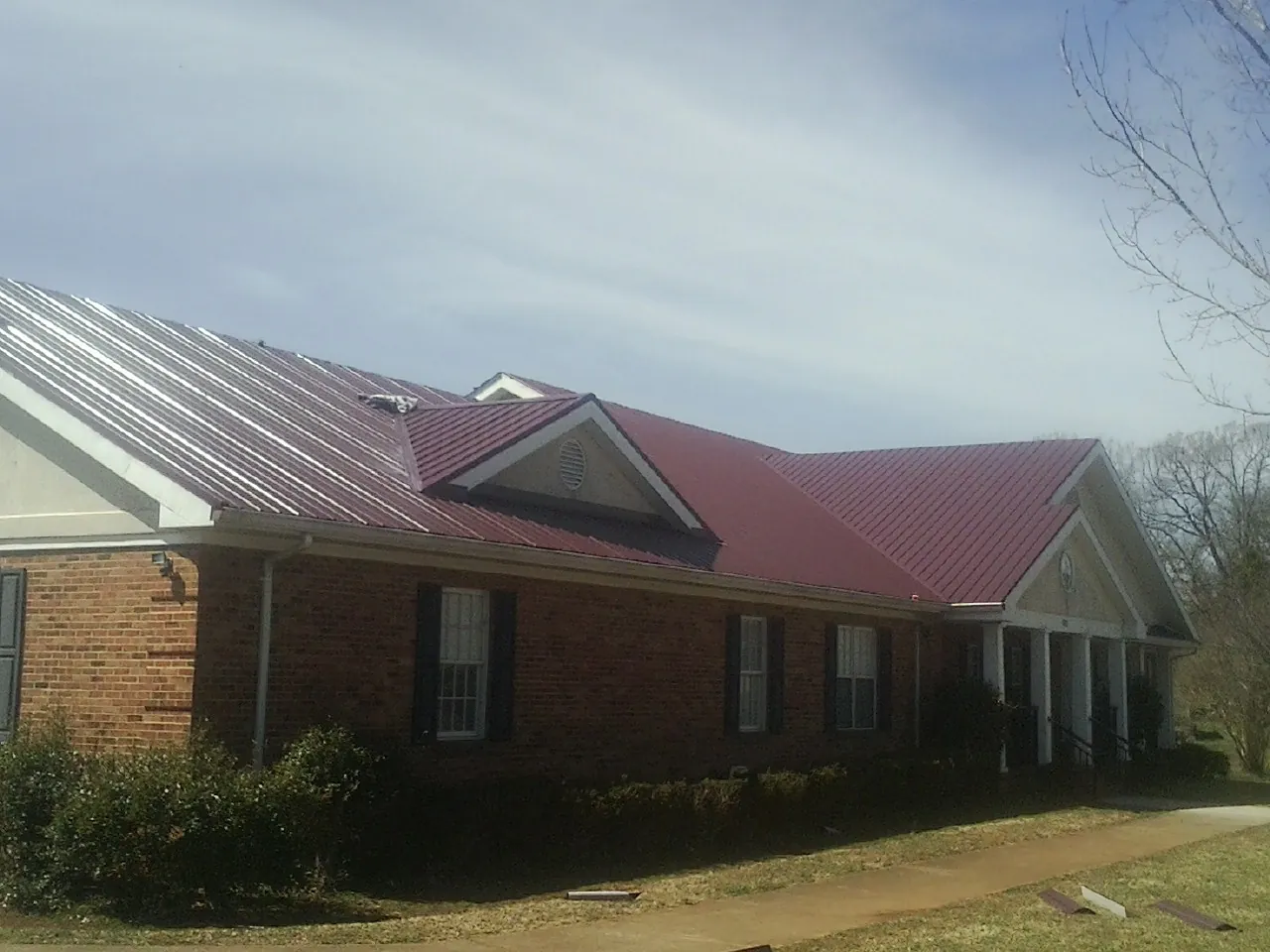Red metal roof with gabled entries on a long brick building, from a Hail Damage Roof Repair job in Eastanollee