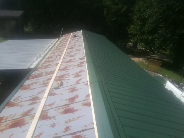 Old rusted panels beside newly installed green metal roofing — Wind Damage Roof Repair by Roofing Brothers in Eastanollee