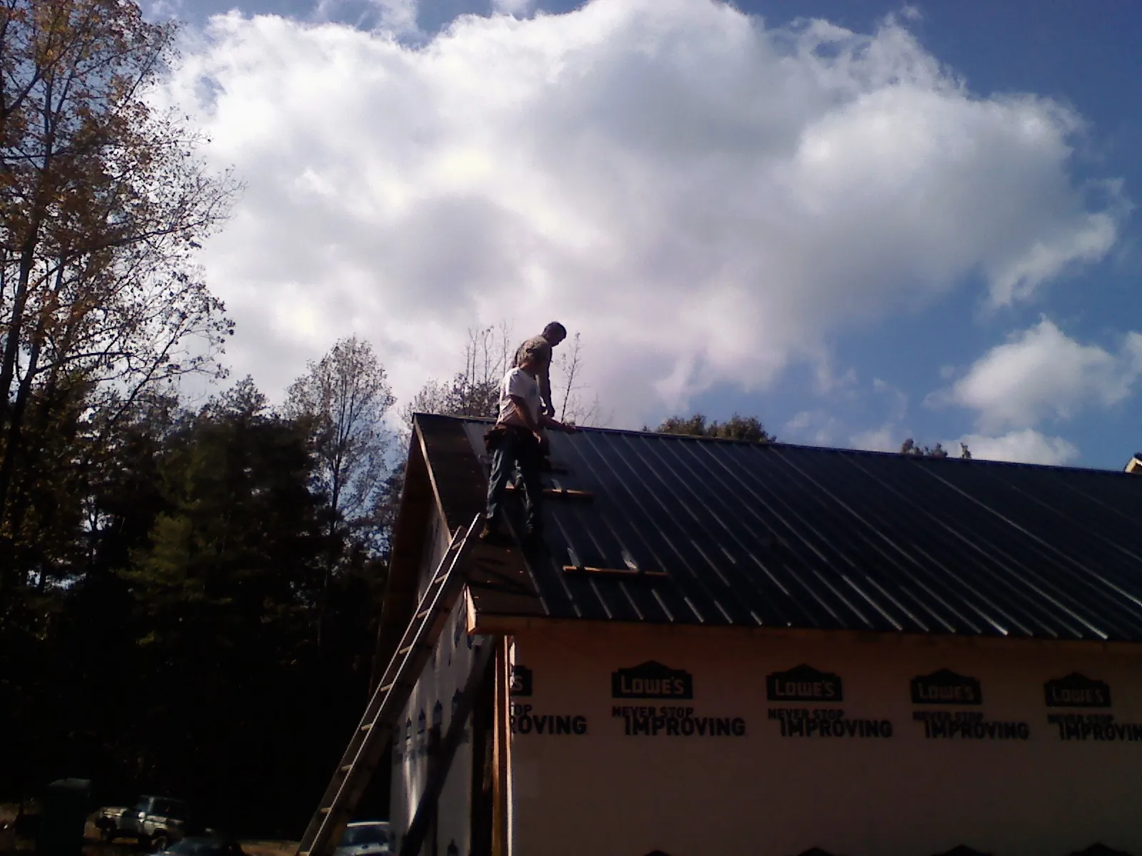 Roofer fastening dark metal panels high against a cloudy sky, from a Roof Inspection job in Eastanollee