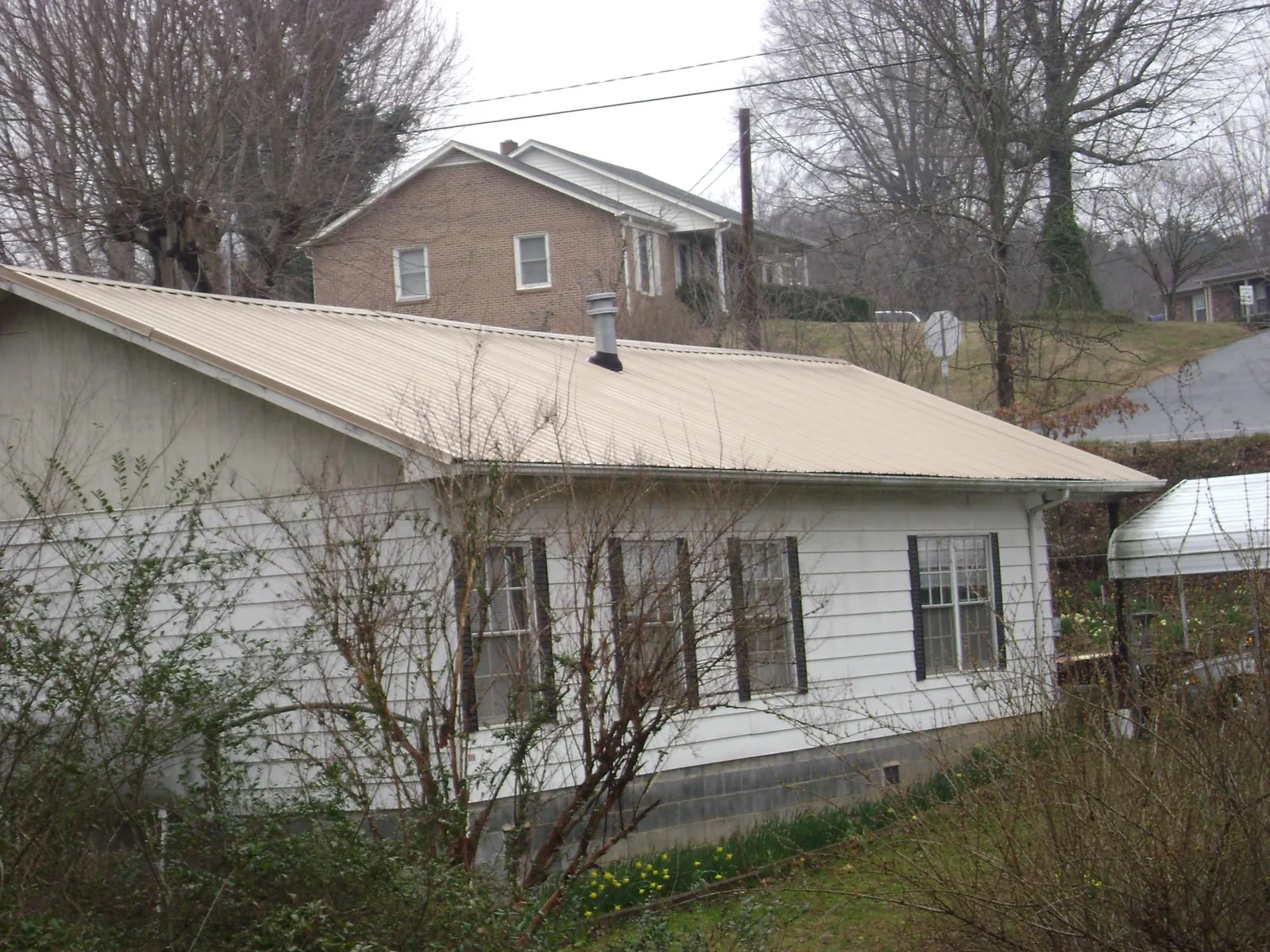 Tan metal roof on a white sided house set into a hillside — Commercial Roofing by Roofing Brothers in Eastanollee
